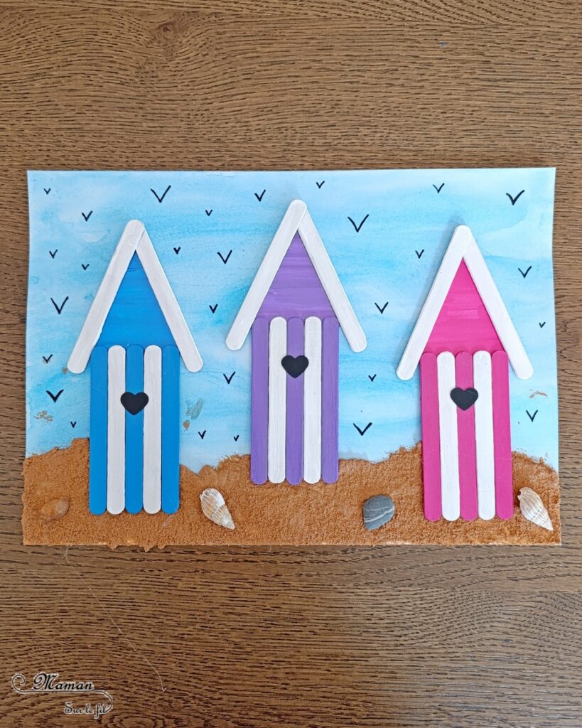 Créer des cabanes de plage avec des bâtonnets de glace en bois : activité créative, récup', peinture et manuelle enfants - Peindre les bâtonnets de bois en blanc et en couleur - Cabanes de plages rayées en récup'- Ouverture en forme de coeur - Collés sur un fond peint à l'aquarelle bleue pour le ciel et peinture marron + sable pour le sable - Effet de volume et de texture - Coquillages en décoration - Dessin et graphismes pour les oiseaux - Bricolage facile et rapide - Thème été, vacances, plage, mer - Bricolage et décoration sympa et facile - Arts visuels maternelle et élémentaire - Cycles 1 et 2 - Créativité - tutoriel photos - mslf
