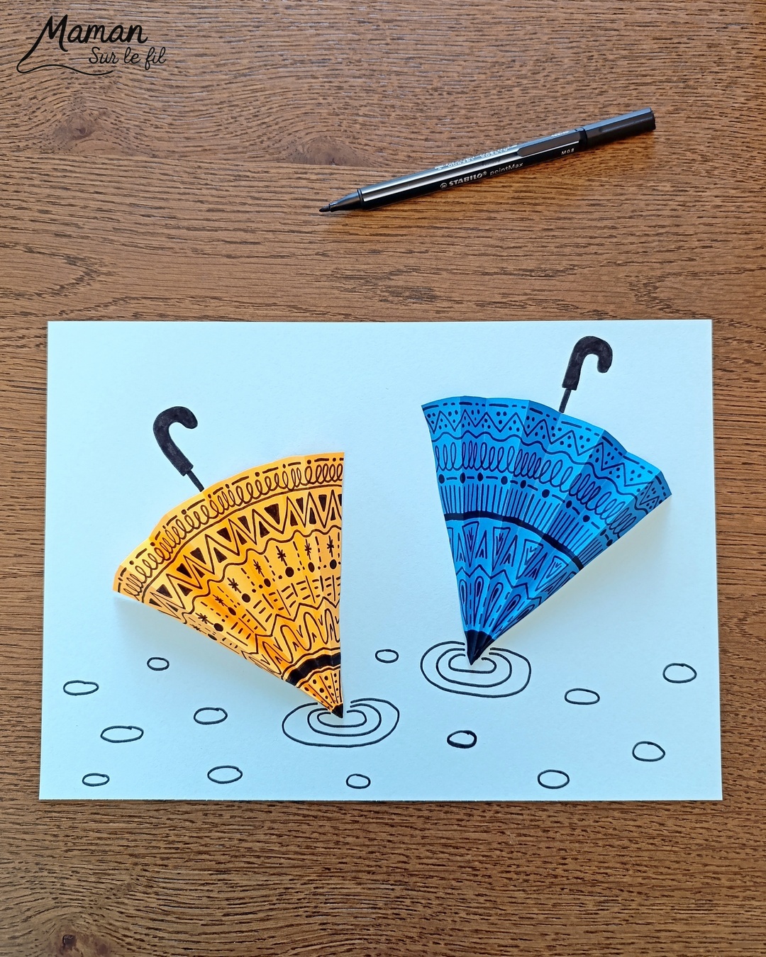 Créer des parapluies graphiques en volume : activité créative, papier et manuelle enfants - Dessin de cercles au compas - Graphismes et dessins noirs pour les décors du parapluie - Découpage et pliage pour l'accordéon - Collage et dessins pour donner l'impression que les parapluies sont posés sous la pluie - Traits obliques - Bricolage et décoration DIY et facile - Bricolage Fait maison, décoration - Thème Météo, Pluie, Nuage, Ciel, Automne - Bricolage sympa et facile - Arts visuels Maternelle et cycle 2 - Maternelle et élémentaire - Créativité - Cycle 1 ou 2 - tutoriel photos - mslf