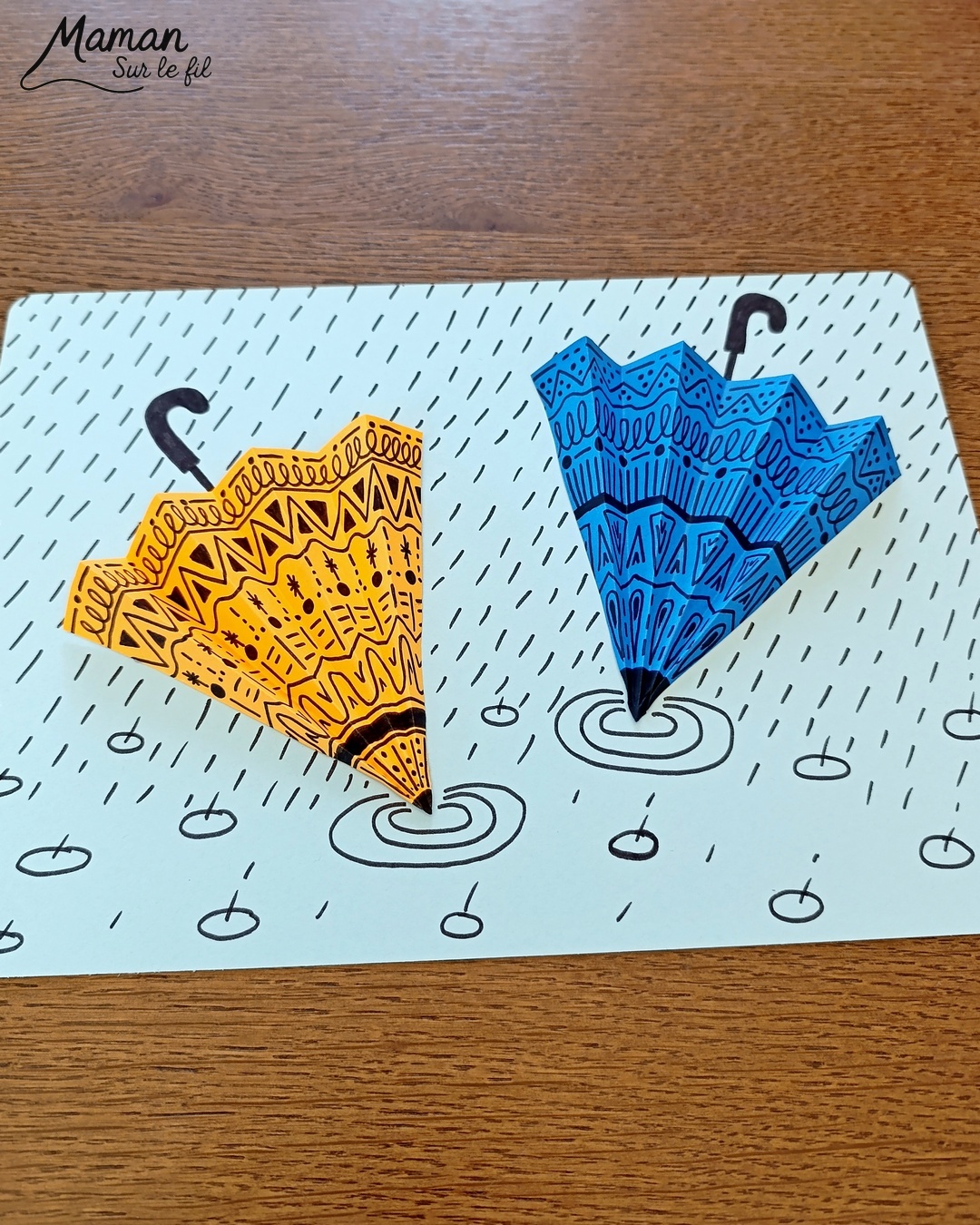 Créer des parapluies graphiques en volume : activité créative, papier et manuelle enfants - Dessin de cercles au compas - Graphismes et dessins noirs pour les décors du parapluie - Découpage et pliage pour l'accordéon - Collage et dessins pour donner l'impression que les parapluies sont posés sous la pluie - Traits obliques - Bricolage et décoration DIY et facile - Bricolage Fait maison, décoration - Thème Météo, Pluie, Nuage, Ciel, Automne - Bricolage sympa et facile - Arts visuels Maternelle et cycle 2 - Maternelle et élémentaire - Créativité - Cycle 1 ou 2 - tutoriel photos - mslf