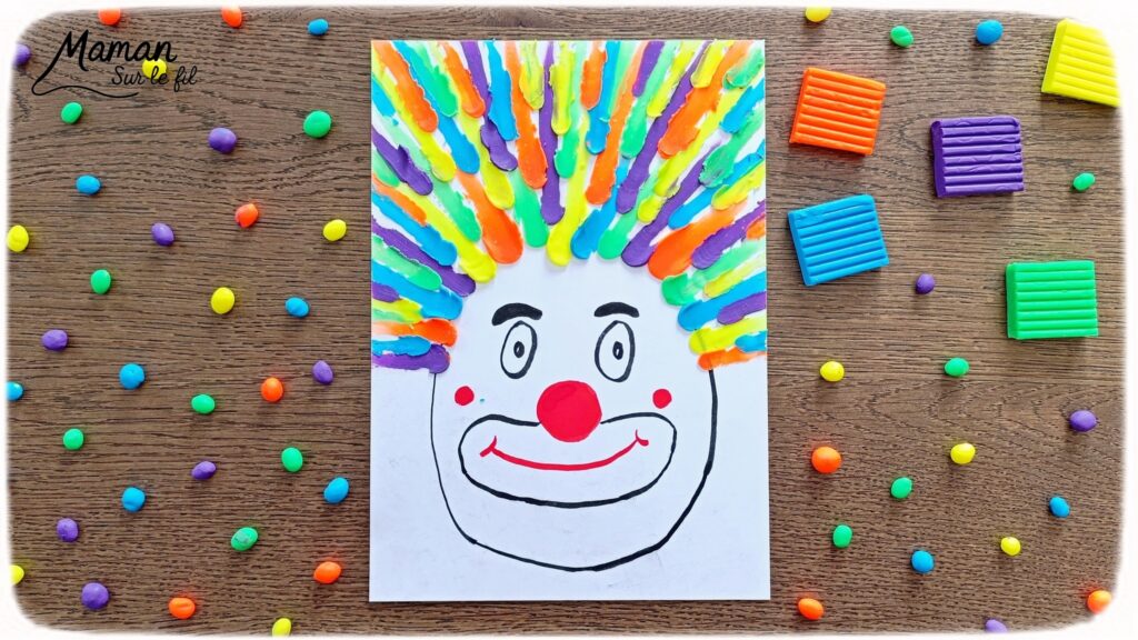 Créer un clown aux cheveux fous en pâte à modeler fluo étalée au doigt : activité créative, sensoriel et manuelle enfants - Dessin d'une tête de clown aux feutres noir et rouge - Cheveux multicolore créés en étalant des boules de pâte à modeler - Motricité fine, musculation des doigts, sensoriel - Bricolage facile, coloré et rigolo - Thème Carnaval, Mardi-Gras, cirque, anniversaire et fêtes - Bricolage et décoration sympa et facile - Arts visuels maternelle et élémentaire - Cycles 1 et 2 - Créativité - tutoriel photos et vidéo - mslf